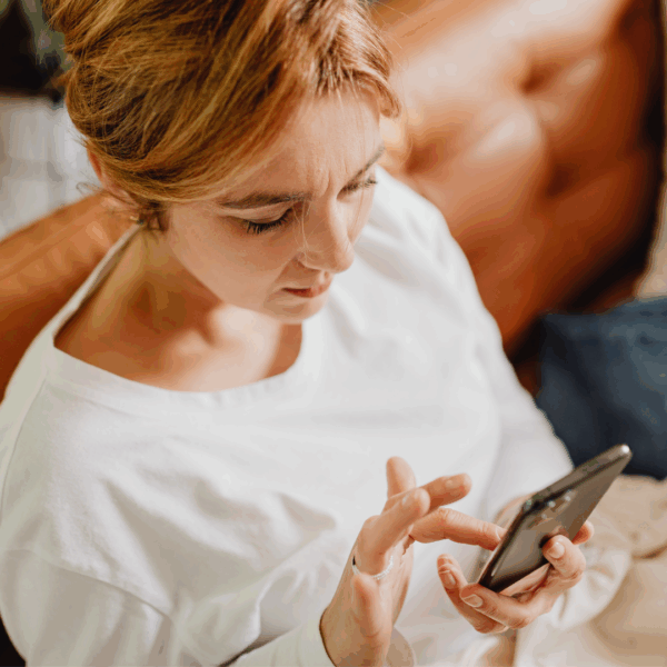 A woman in a white jumper sits on brown sofa, using her mobile phone.