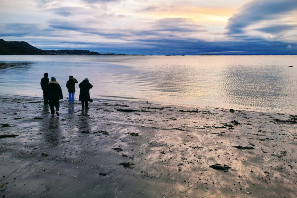 A small group of people stand on a beach looking out over the water.