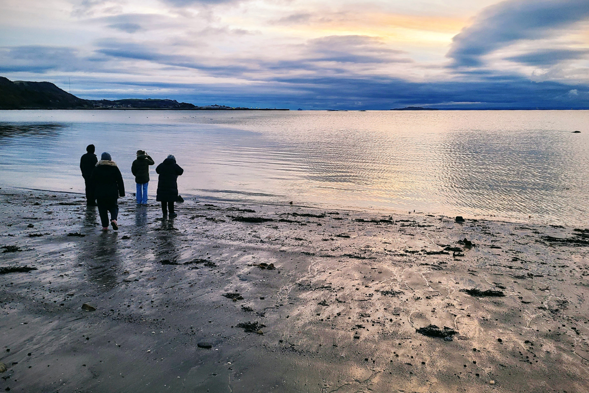 A small group of people stand on a beach looking out over the water.