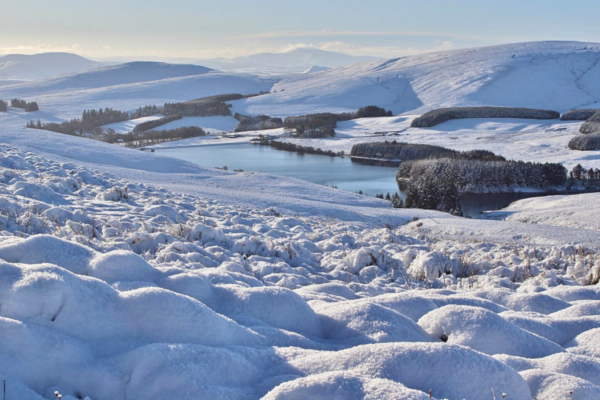 A snow covered valley of rolling hills and woodland.