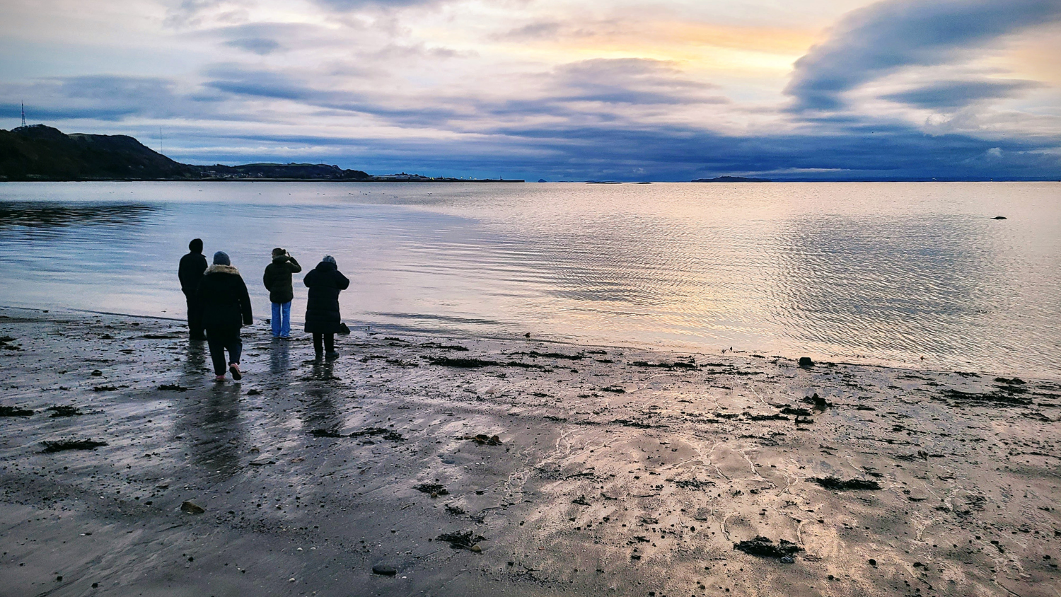 A small group of people stand on a beach looking out over the water.
