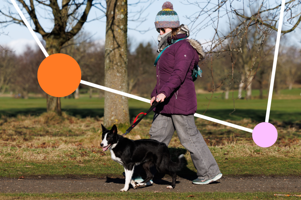 A woman wearing a jacket, scary and bobble hat walks with her dog along a path through a local park.