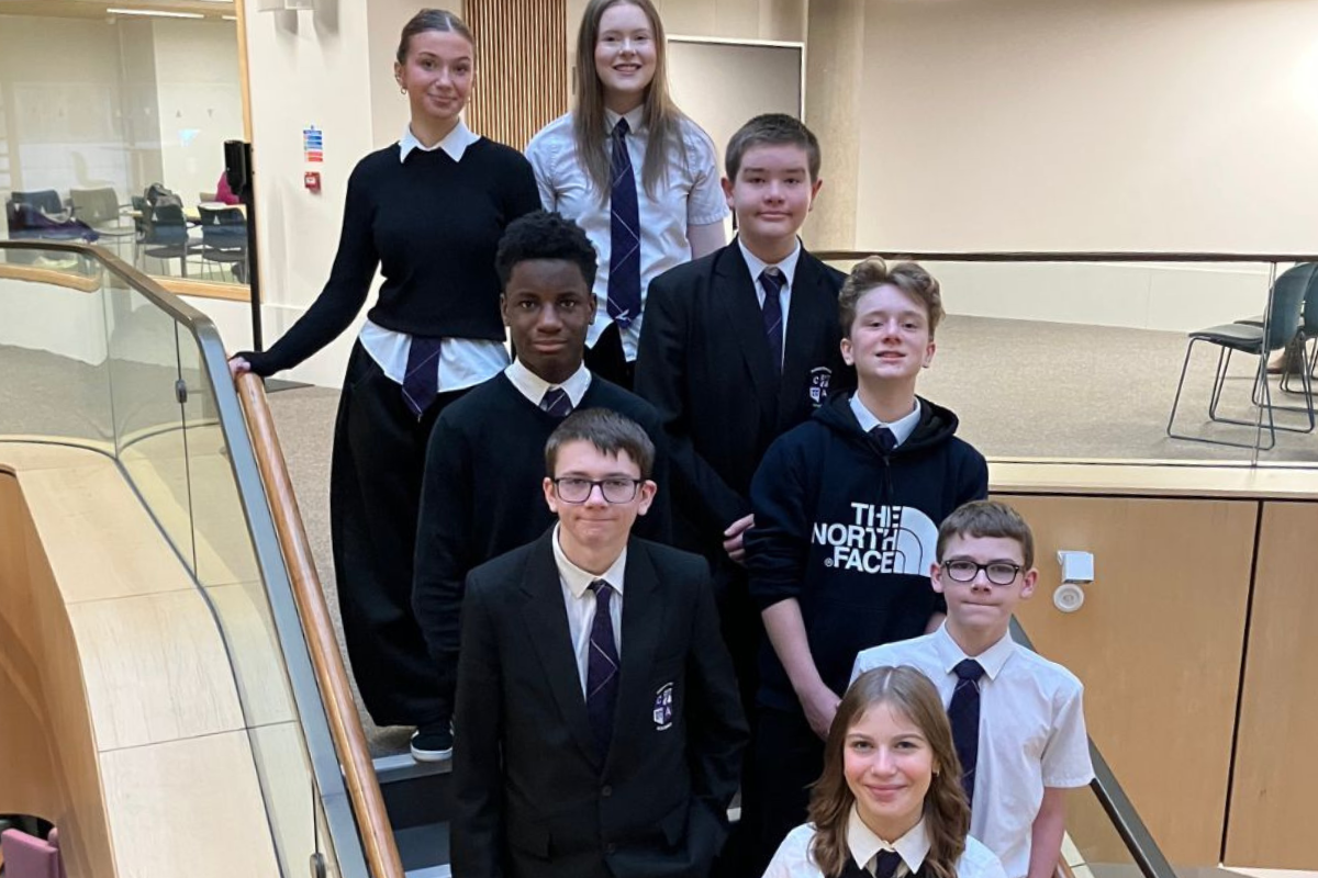A group of boys and girls smile as the stand on a stairwell in a school.
