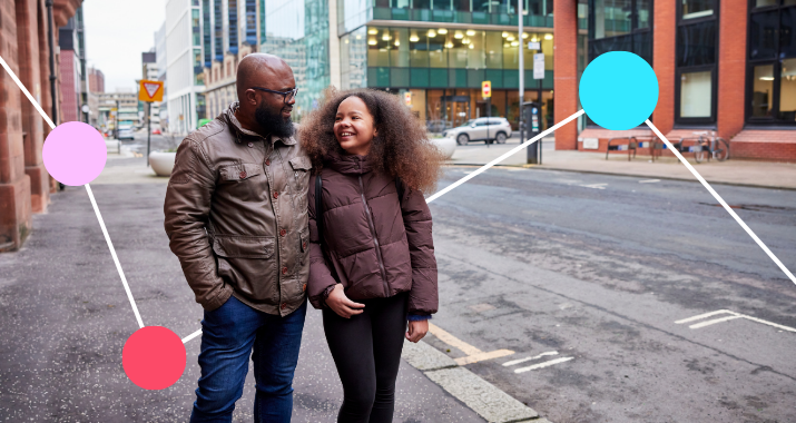 A gentleman smiles as he walks along a city street with his daughter.
