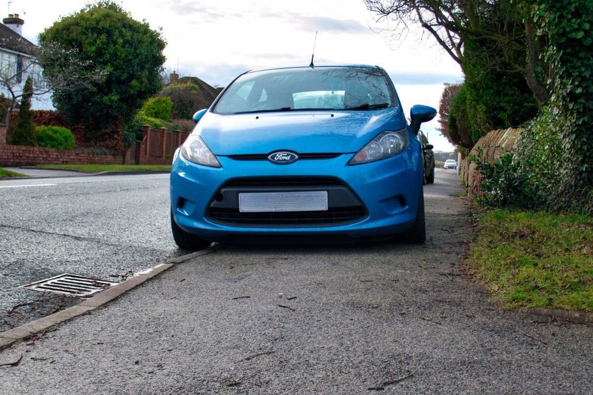 A car parked on the pavement, blocking access.