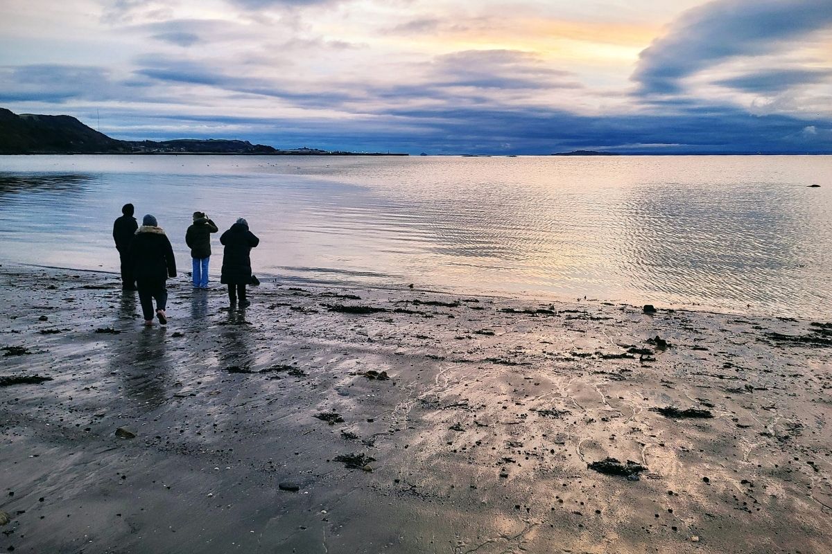 A small group of people stand on a beach looking out over the water.