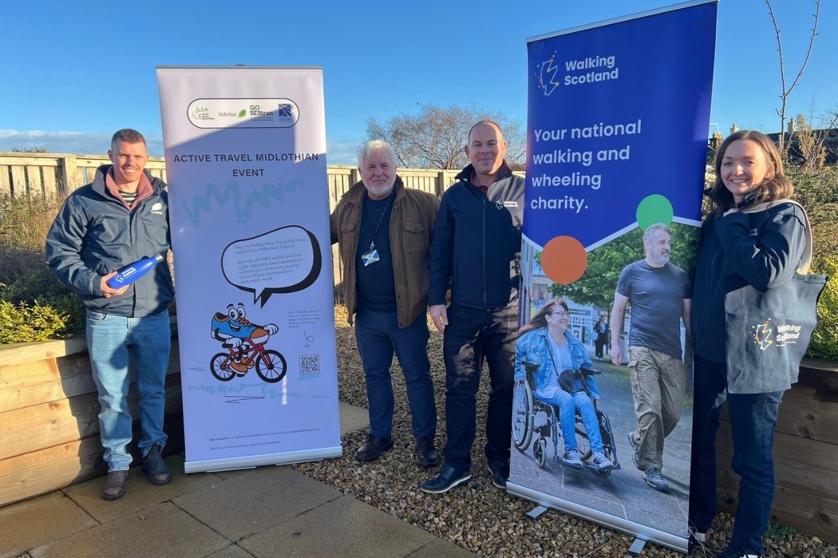 Representatives from the Midlothian Council and Walking Scotland smile as they stand beside branded pop-up banners.