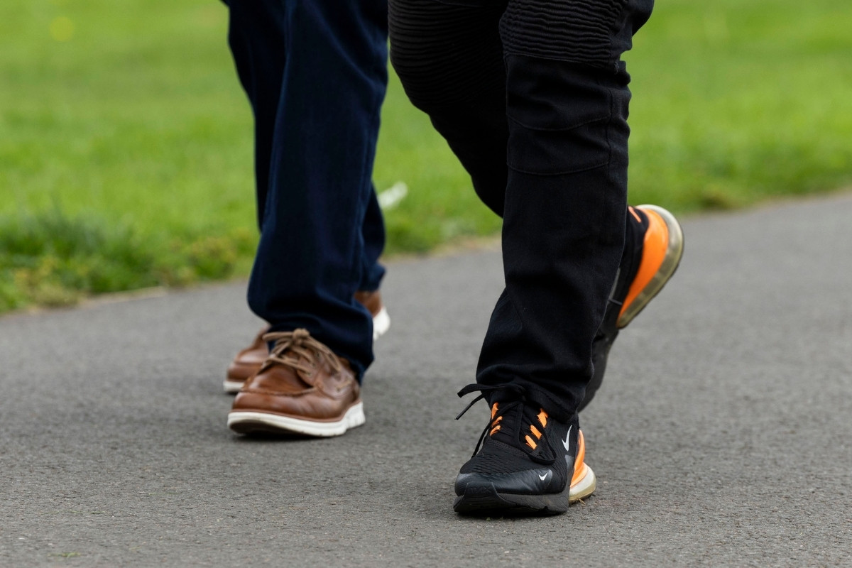 The lower legs and feet of two people walking along a path of a local park.
