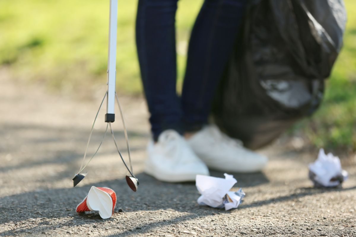 A close up image of someone using a litter pick to pick up rubbish off a pavement.