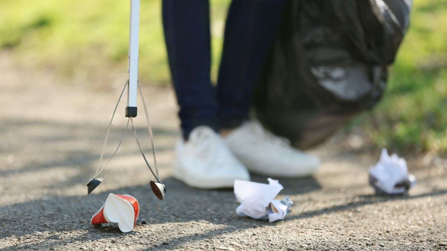 A close up image of someone using a litter pick to pick up rubbish off a pavement.