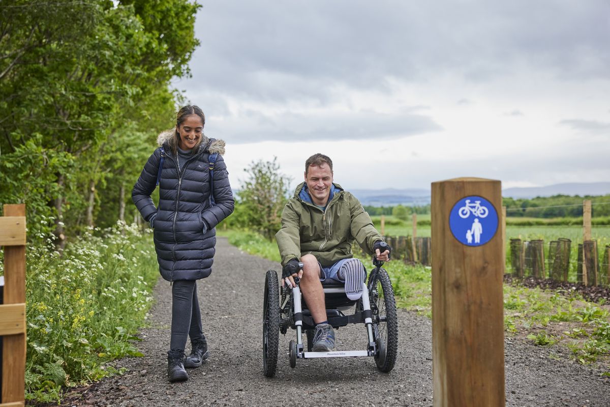 A woman walks alongside a man wheeling in a motorised wheelchair.