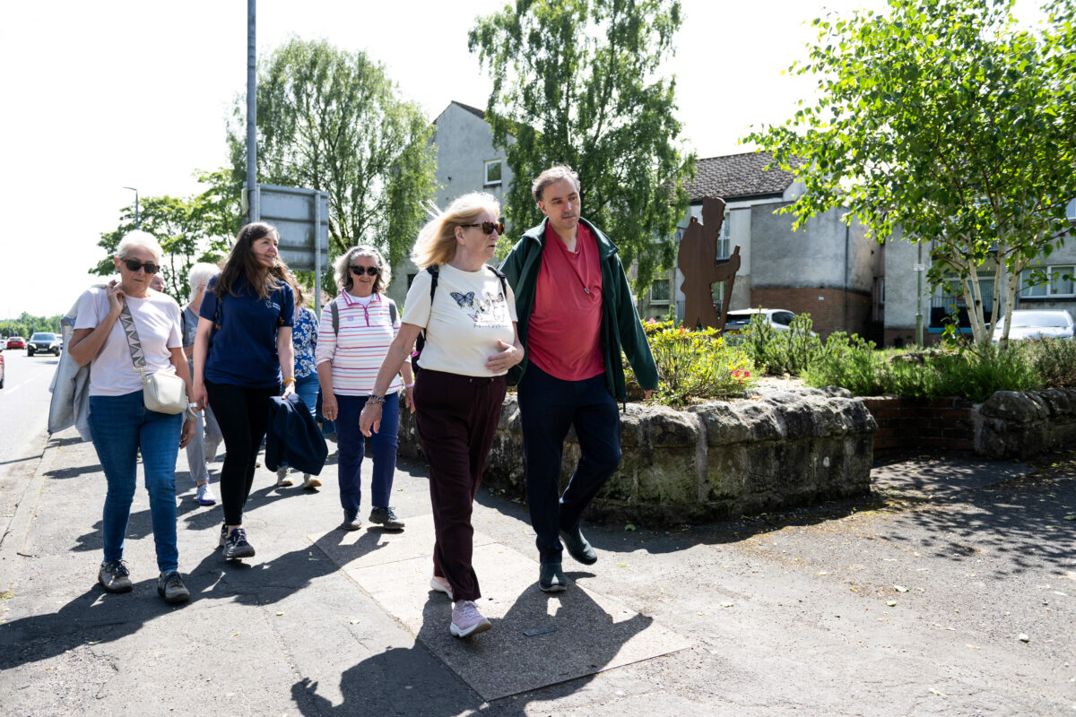 A group walk along a pavement. They are wearing sunglasses and t shirts.